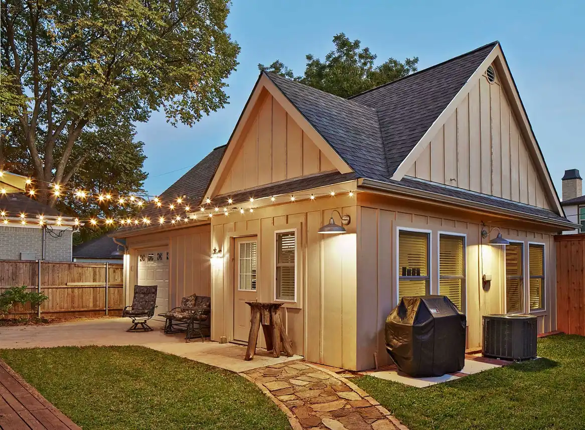 Board-and-batten room addition with string lights in the backyard at dusk